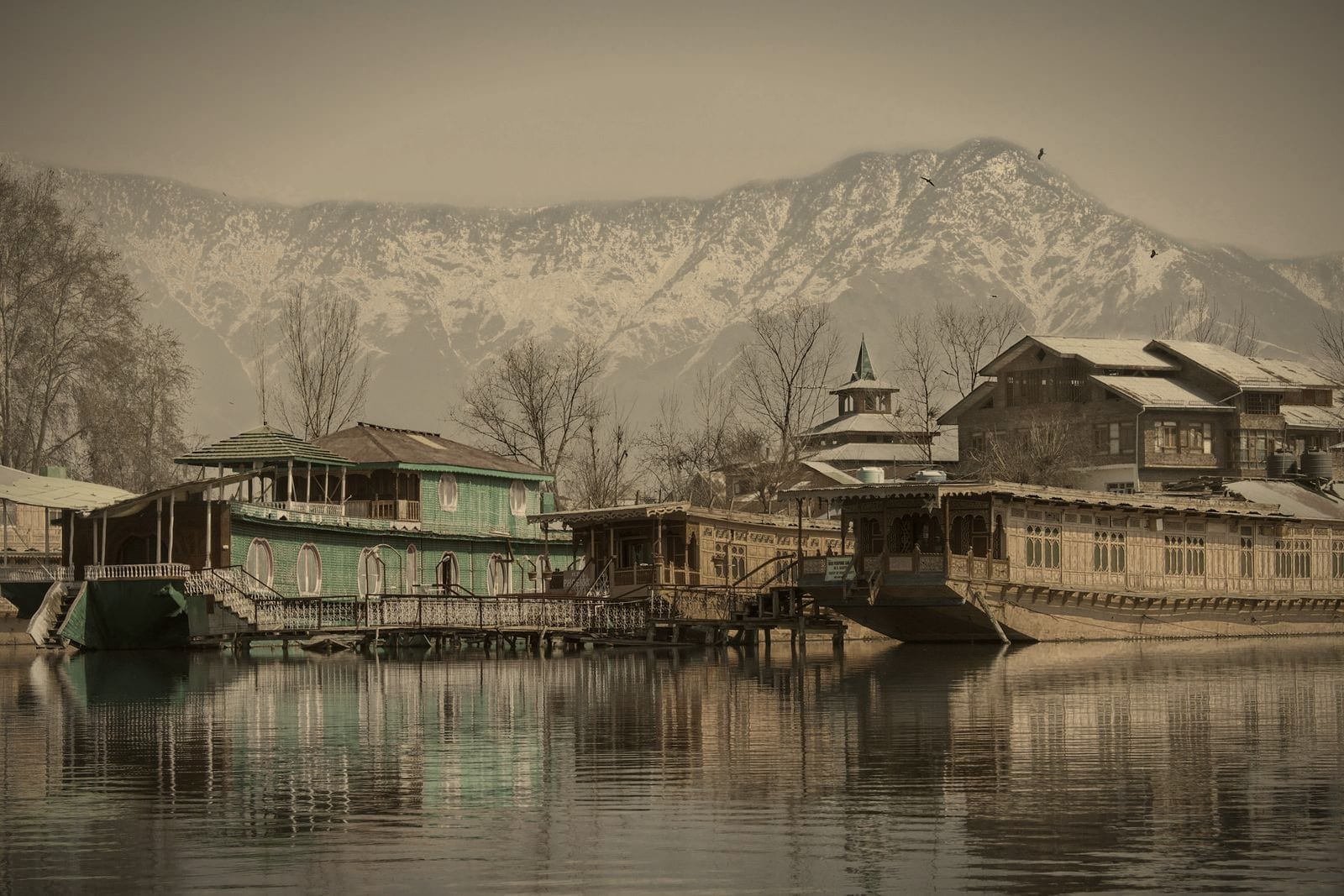 Wooden houseboats on a still lake beneath snow-covered mountains in Srinagar