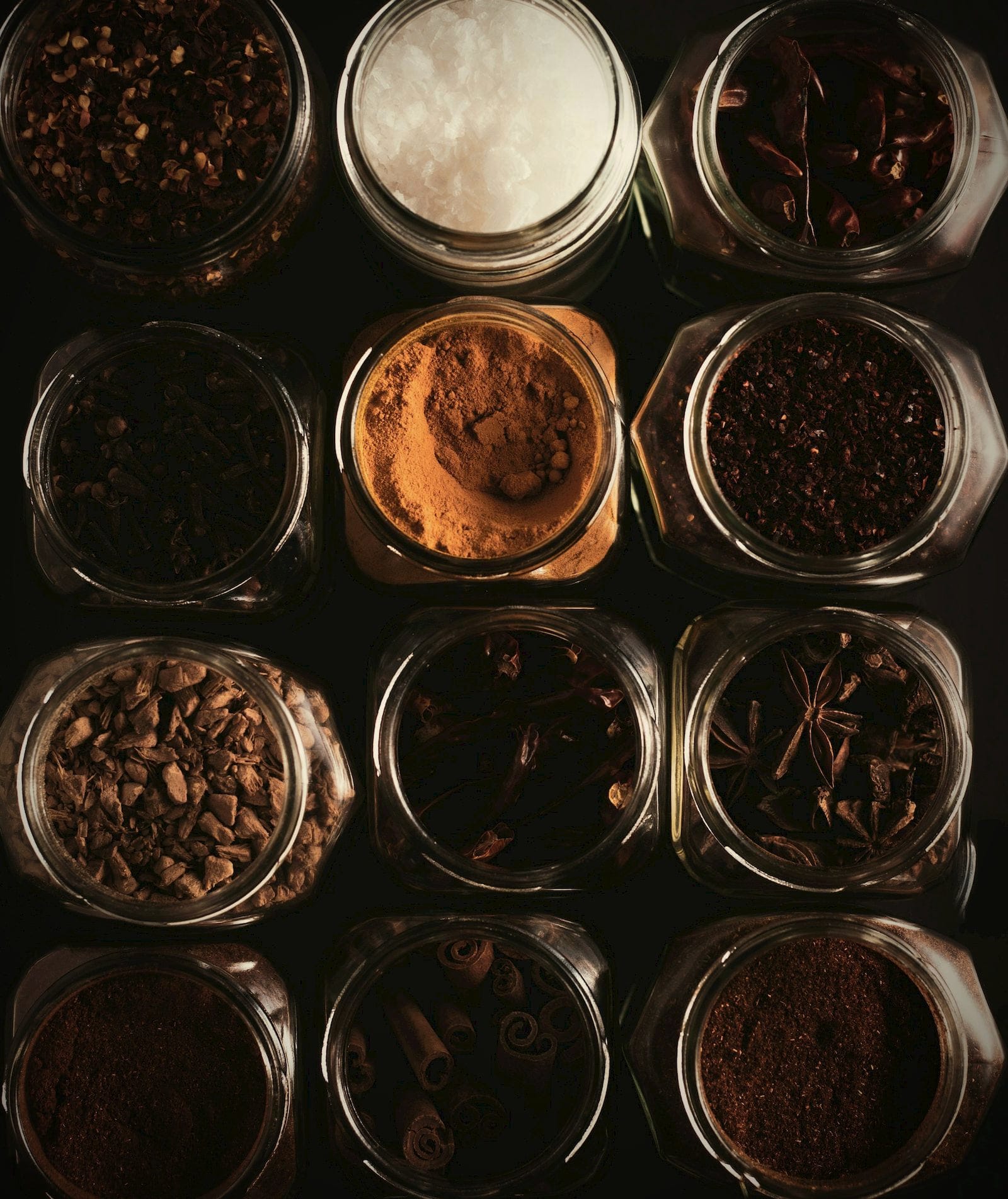 Rows of glass jars holding whole and ground spices, seen from above