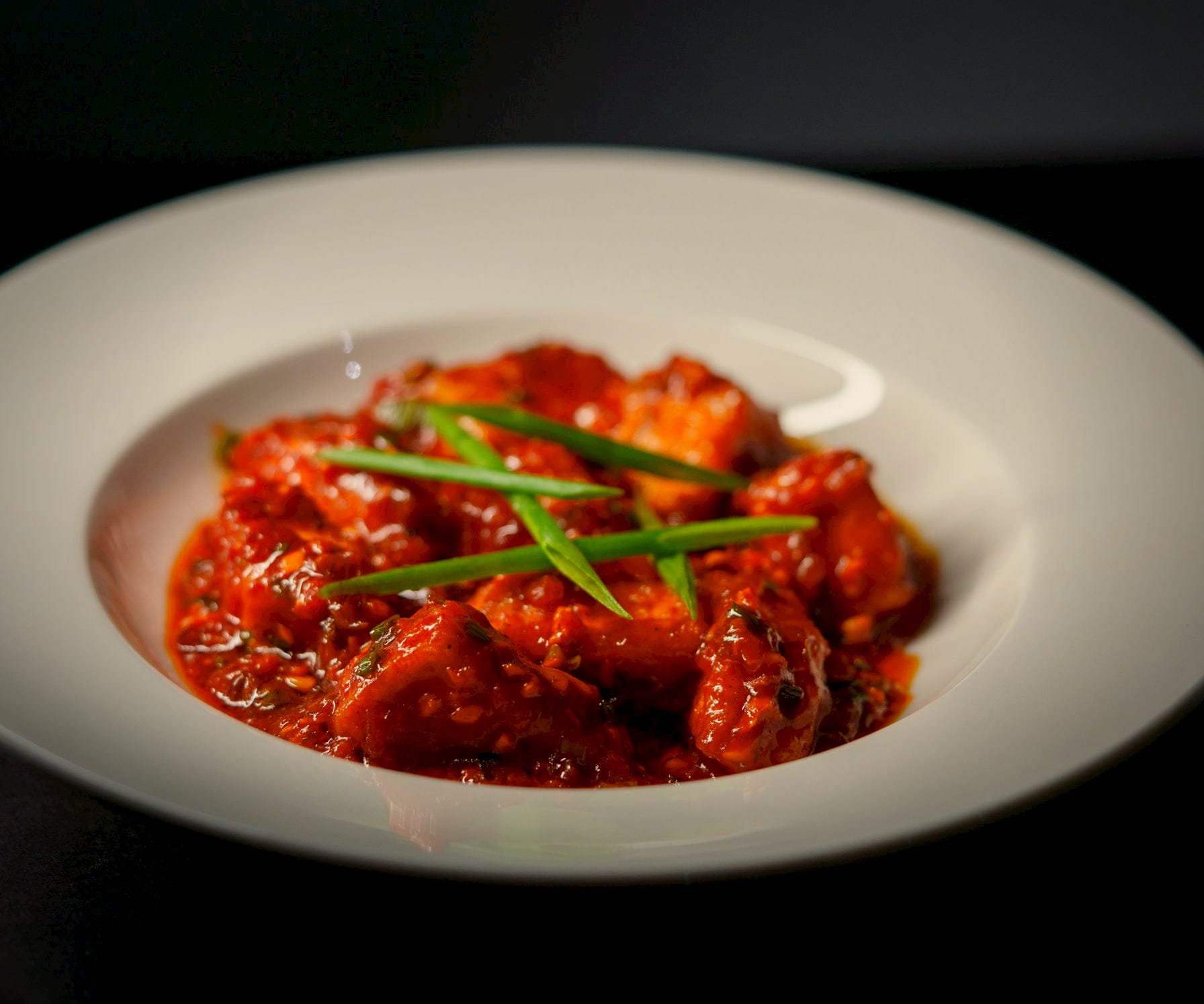 Paneer in a deep roasted red, semi-dry masala glossy with ghee, in a wide ivory bowl