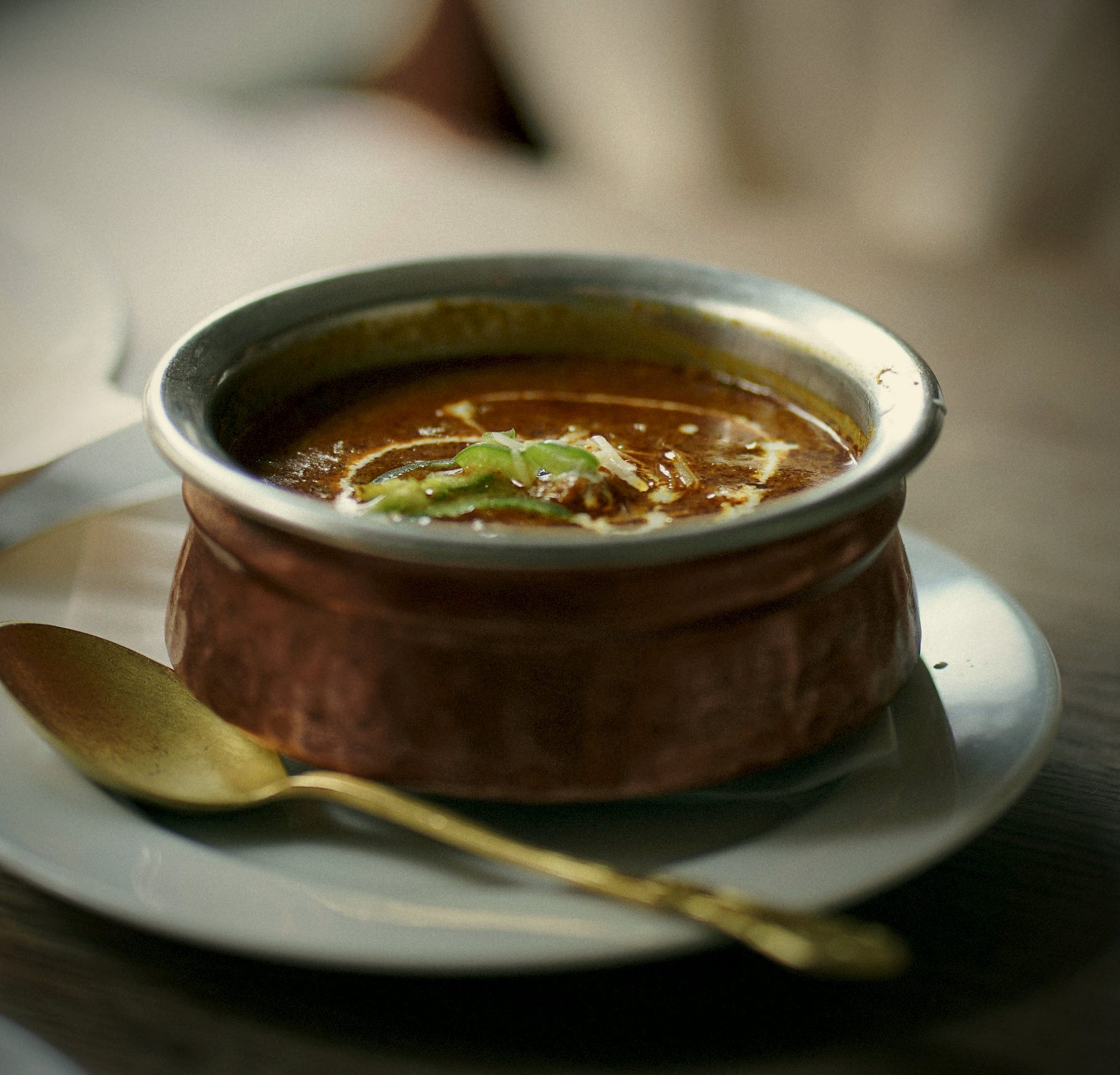 Glossy black dal in a hammered copper handi, with a brass spoon