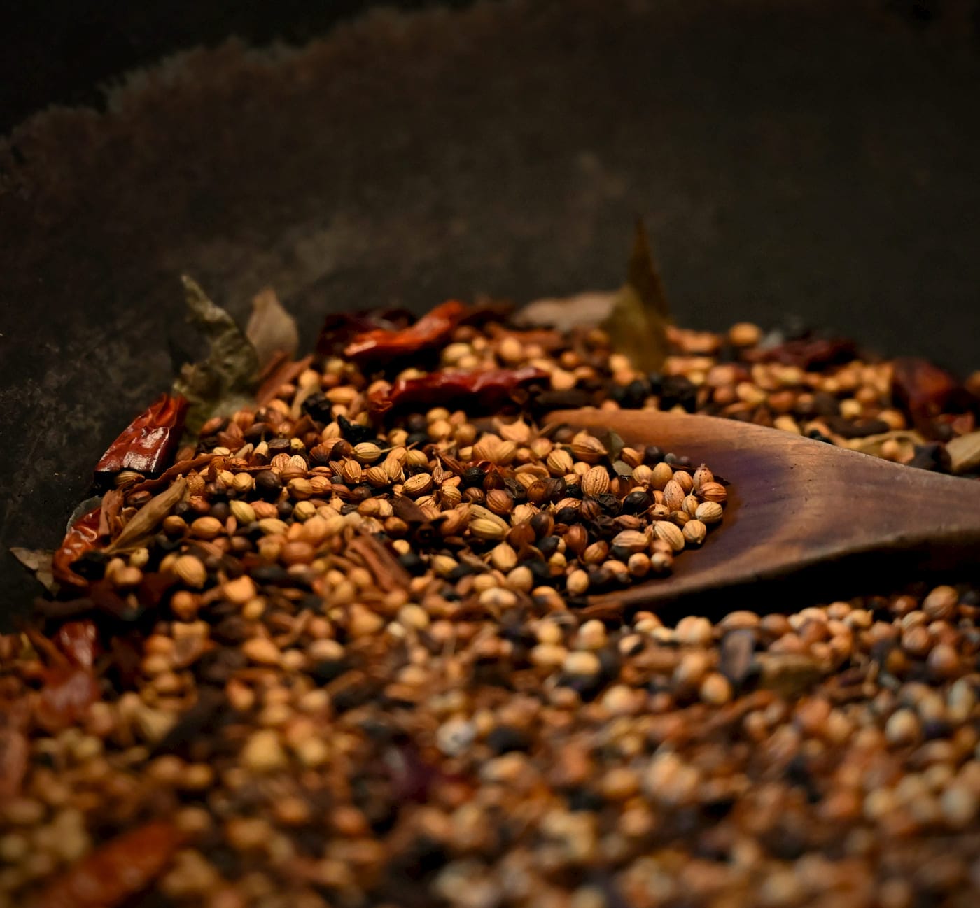 Whole spices dry-roasting in a black pan: coriander seed, black pepper and dried red chillies, turned with a wooden spoon
